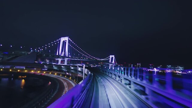 Train window view of approaching the illuminated Rainbow Bridge at night in Tokyo, Japan