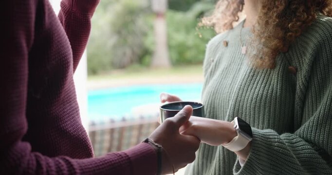 Couple exchanging dark ceramic mugs at doorway to backyard pool, sparking chat while showing watch
