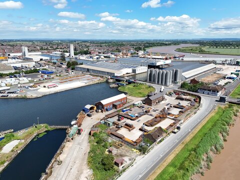 Aerial view of the industrial port area featuring warehouses, storage silos, and the river Ouse under a blue sky in Goole, England, United Kingdom.