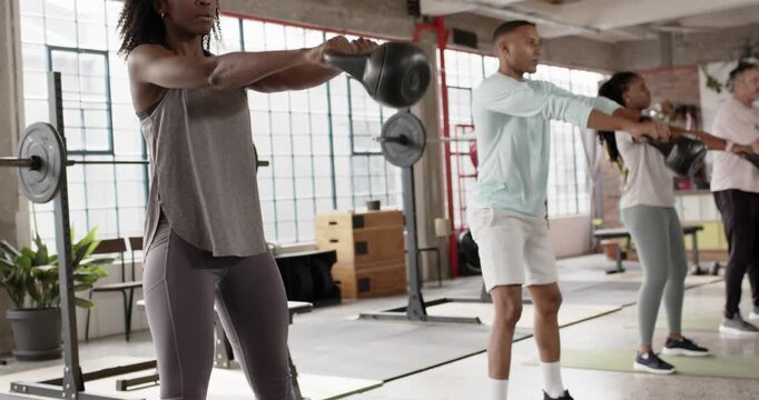 Diverse friends in sportswear hinging and driving hips, powering kettlebell swings on mats in class