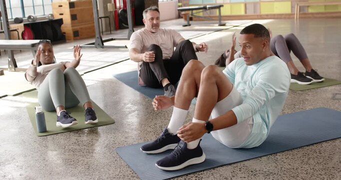 Diverse group following man on blue mat leading tempo, doing crunches in gym for core