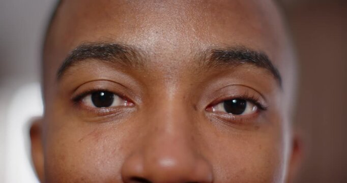 Adult African male holding gaze into camera in room, reacting to ring light, smiling warmly