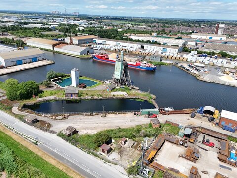 Aerial view of the industrial port area in Goole, featuring a cargo ship in the canal, warehouses, storage yards, and green landscape. Goole, England, United Kingdom.