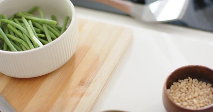 Camera panning right, white ribbed bowl of green beans on cutting board, revealing nuts and berries