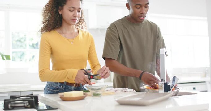 Couple making dinner on island woman cutting herbs African American man rinsing veg in colander
