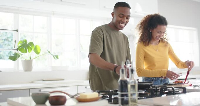 Diverse couple cooking at kitchen island, smiling, man moving bowl, woman stirring with red spatula