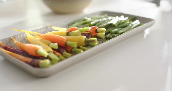 Camera pulling in, racking focus on tray of carrots and stalks on white counter, showing freshness