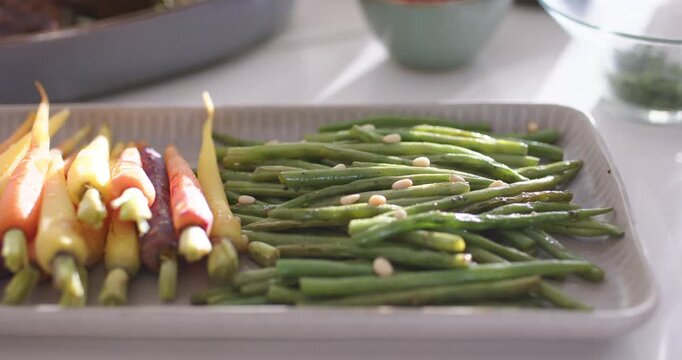 Camera is pulling focus to sharpen green beans and nut garnish on ceramic platter on countertop