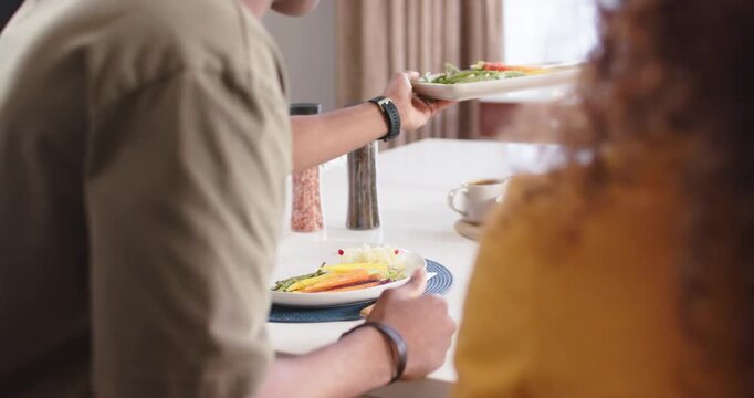 Couple watching man serving vegetables from platter onto white plate on blue placemat