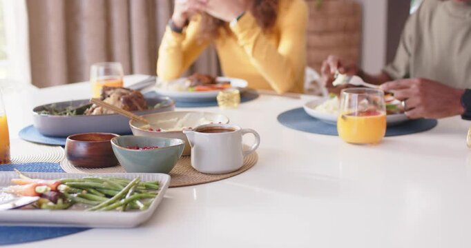 Couple sitting at dining table, man starting eating with fork, woman gesturing while sharing meal