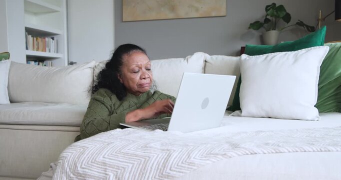 Senior African American woman checking bill on laptop at home holding card, calling, closing laptop