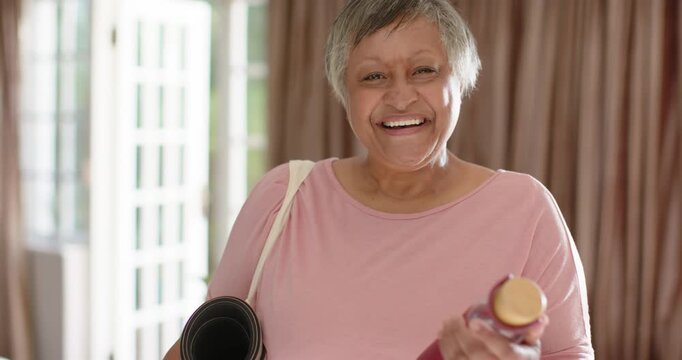 Mature African woman facing camera by doors shifting mat rotating bottle showing gold cap with tote