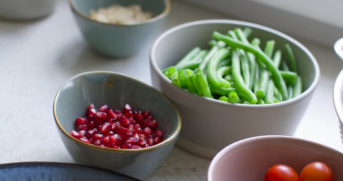 Camera is shifting frame around bowls on countertop, pulling focus to center green beans and arils