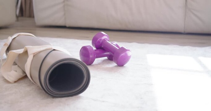 Sunlight is shifting, causing patch while gray mat, strap and purple dumbbells are remaining on rug