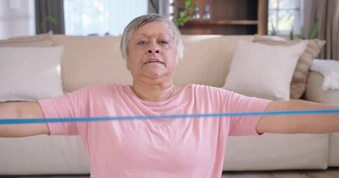 Woman sitting before sofa after placing blue resistance band across chest, pulling for fitness