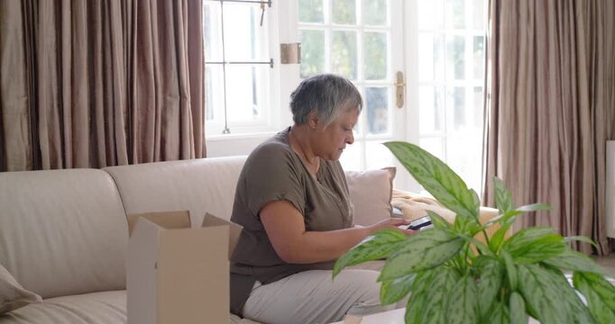 Senior African American woman opening box on sofa, scanning white bottle with red cap using phone