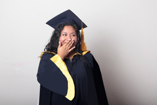 Young, dark-haired Latina woman dressed in a cap and gown is happy and excited to celebrate her graduation