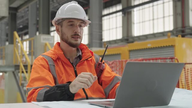 Technician uses laptop and radio during maintenance depot operations at Train Depot facility, inspecting modern factory equipment with white hard hat and orange safety suit.