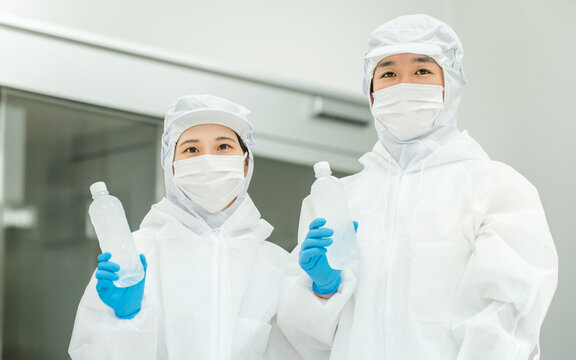 水工場,飲料メーカーで働くペットボトルの水を持つ防塵服姿の製造スタッフ