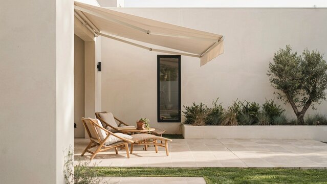 Patio terrace features comfortable lounge chairs placed under a modern retractable awning against a white wall.