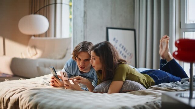Teen lovers using smartphones chilling loft bedroom. Young couple discussing