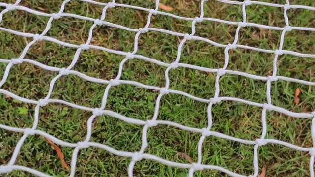 Close up of white soccer goal net texture with green grass background. Football gate netting mesh grid pattern on a sports field or backyard lawn.