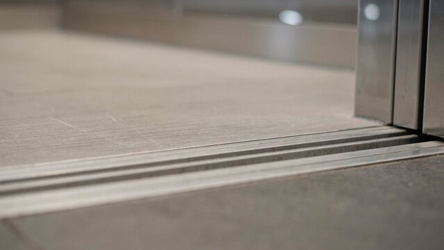 Elevator door threshold sits flush with the tiled office floor highlighting the sliding track of a modern lift cabin.
