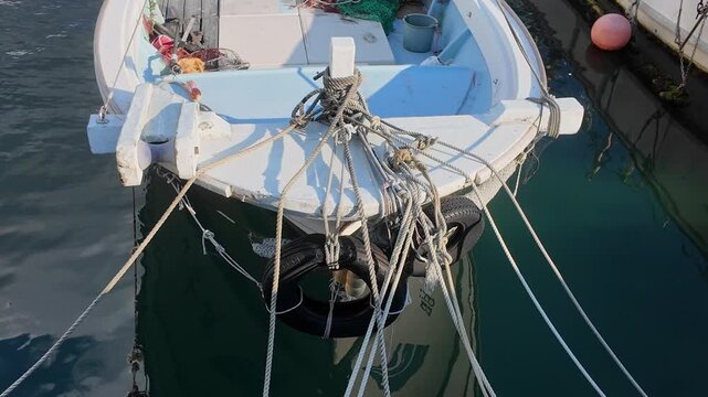 Front view of a small wooden fishing vessel with a tire fender floating on clear blue water.