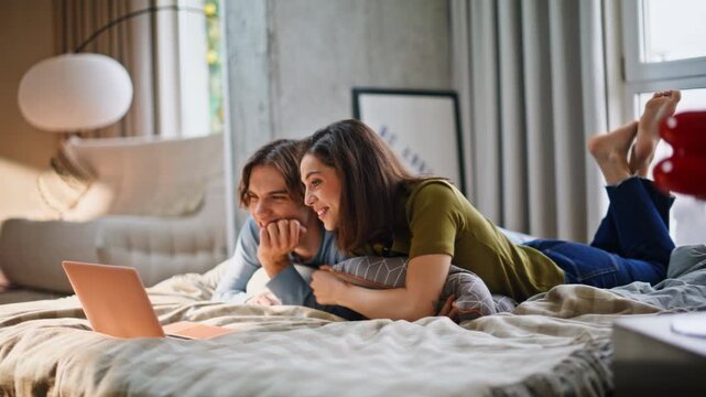 Home couple looking laptop lying modern bedroom. Newlyweds watching comedy show