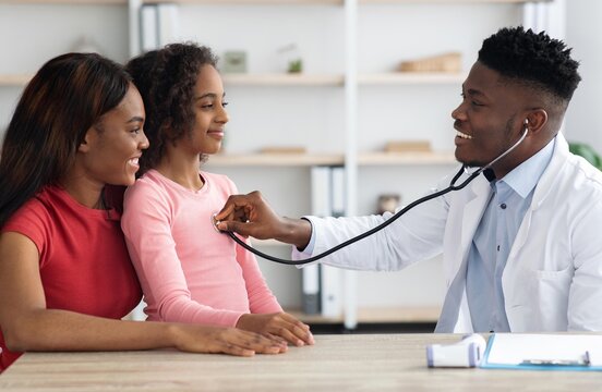 Smiling Doctor Examining Young Girl In Pink Top With Stethoscope While Mother Watches, At Pediatric Clinic. Positive Healthcare Interaction Promoting Child Wellness In A Friendly Environment.