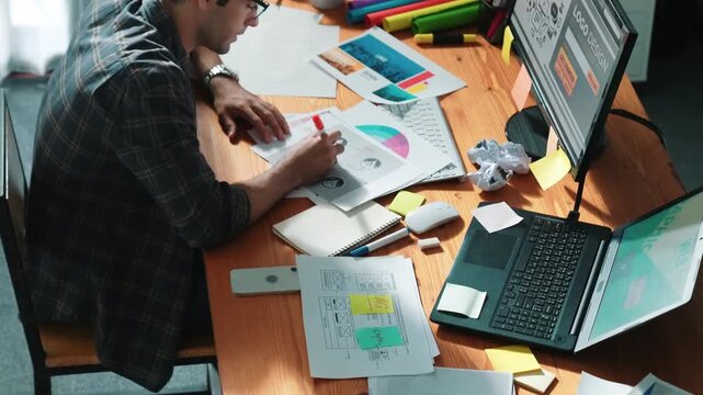 Professional designer writing and designing logo graphic at meeting. Closeup of business man working on colored palettes and writing idea on sticky notes on table with equipment and paper. Symposium.