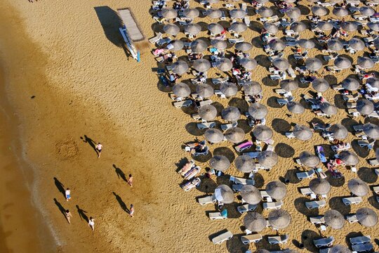 Aerial view of Kilyos shore featuring rows of sun umbrellas on the sandy beach with people walking along the water in Sariyer, Istanbul, Turkey.