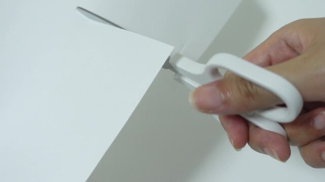 Close-up footage of scissors cutting white paper on clean white background