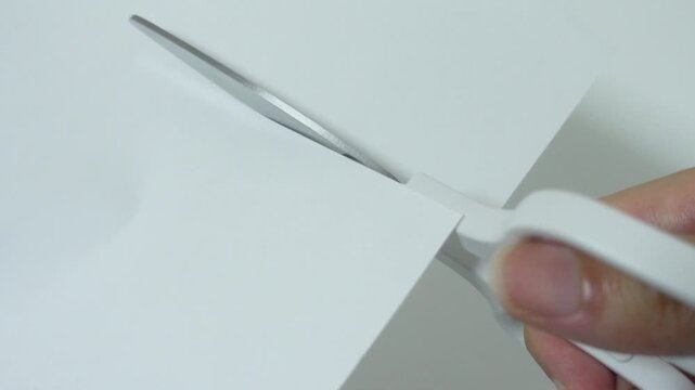 Extreme close-up of scissors blade cutting white paper, craft DIY footage