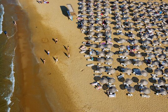 Aerial view of Kilyos shore with rows of sun umbrellas on the sandy beach and people walking along the water in Sariyer, Istanbul, Turkey.