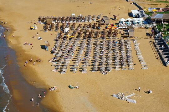 Aerial view of Kilyos shore with rows of beach umbrellas and sun loungers on the sand with people walking along the water in Sariyer, Istanbul, Turkey.