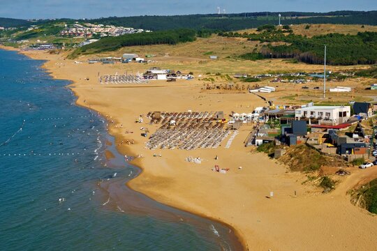 Aerial view of Kilyos shore with sandy beach, rows of sun loungers, beach clubs, and calm blue sea in Sariyer, Istanbul, Turkey.
