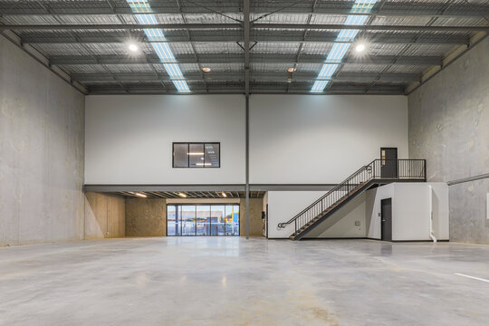Modern industrial warehouse interior featuring high clearance ceilings, mezzanine office space, concrete flooring and contemporary construction. Suitable for logistics, warehousing and distribution.