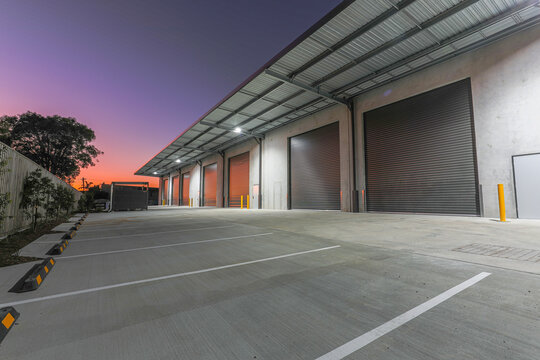 Industrial loading bays and roller doors at twilight with parking area and warehouse access. Ideal for logistics, freight and distribution concepts