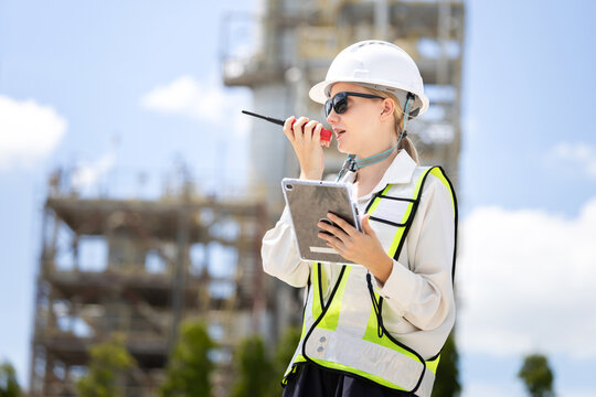 Female engineer with walkie talkie and tablet at oil refinery plant, Industrial engineer communicating on radio at refinery site, Woman supervisor using digital tablet at modern oil and gas facility