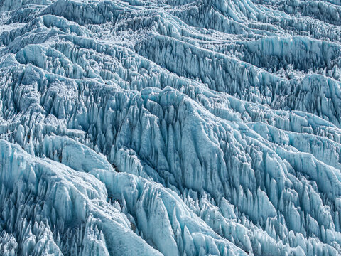 Aerial view of the rugged, icy surface of a glacier in the Himalayas, featuring deep crevasses and jagged blue ice formations in Nepal.