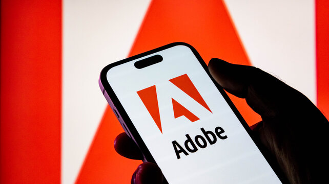 Hand holding a smartphone displaying the adobe logo with a large adobe logo in the background