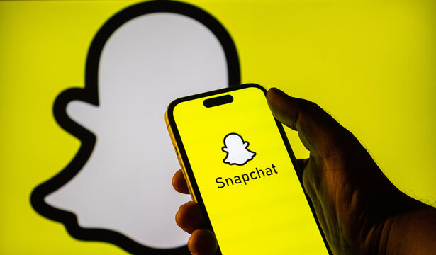 Hand holding a smartphone displaying the snapchat logo with a large snapchat ghost icon in the background