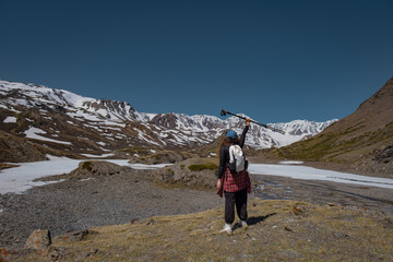 Fototapeta premium Rear view of young woman traveler with backpack raising trekking poles on mountain hill. Female hiker celebrating success and exploring remote scenic wilderness landscape.
