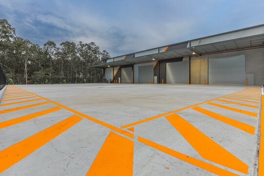 Modern industrial warehouse with loading bays, concrete hardstand and safety markings. Large logistics facility featuring roller doors, loading access and commercial infrastructure.