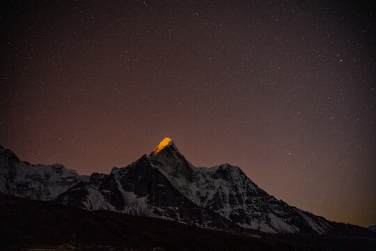 Aerial view of the illuminated peak of Ama Dablam rising against a starry night sky in the Himalayas, Nepal.