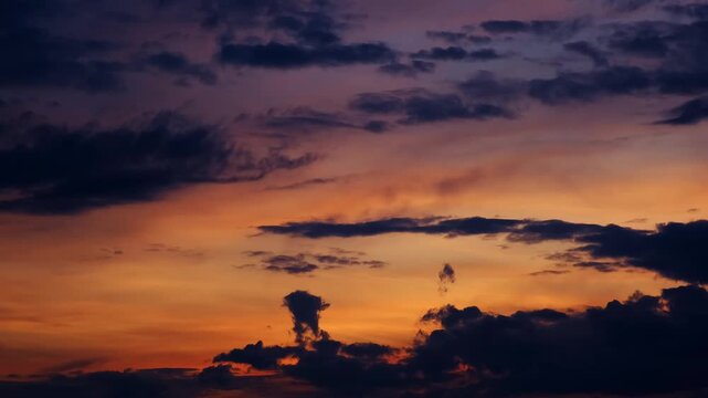 Colorful sunset sky with dark cloud silhouettes and a gradient from deep blue to orange. Bright evening skyscape. High quality 4K footage.