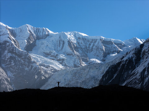 Aerial view of a person standing with arms outstretched on a rocky ridge against the massive snow-covered peaks of the Himalayas in Nepal.