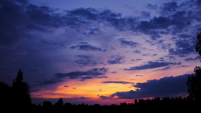 Colorful sunset sky with dark cloud silhouettes and a gradient from deep blue to orange. Bright evening skyscape. High quality 4K footage.