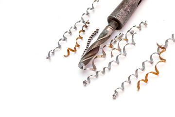 An industrial twist drill bit with a morse taper shank resting under long, spiraled metal shavings on a white background. © Александр Серебрянни